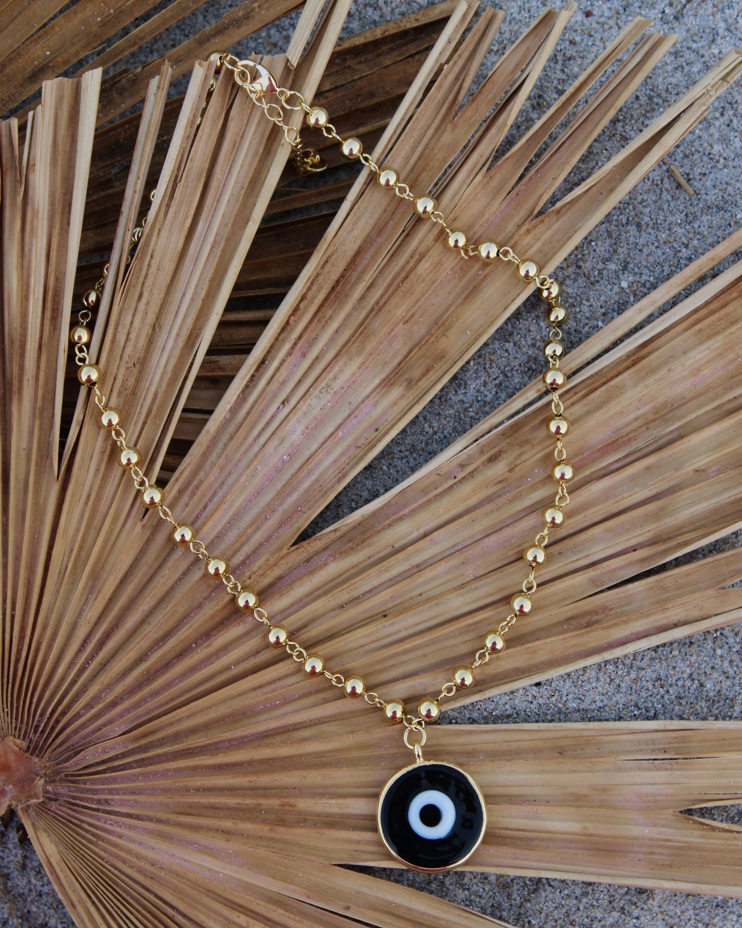Gold beaded necklace with a black eye pendant inside a shell gold plated