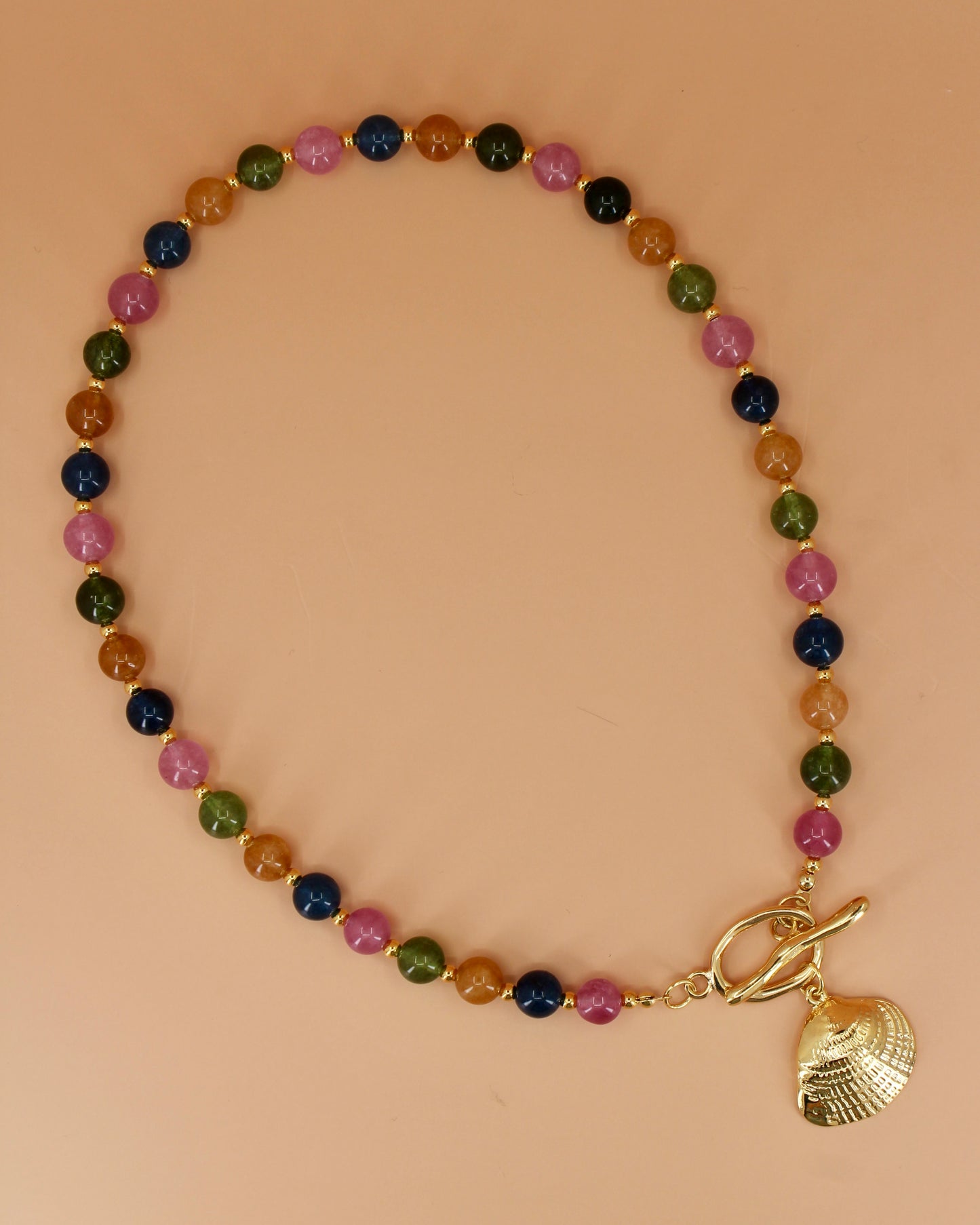 Multicolored beaded bracelet with a gold shell charm on a beige background