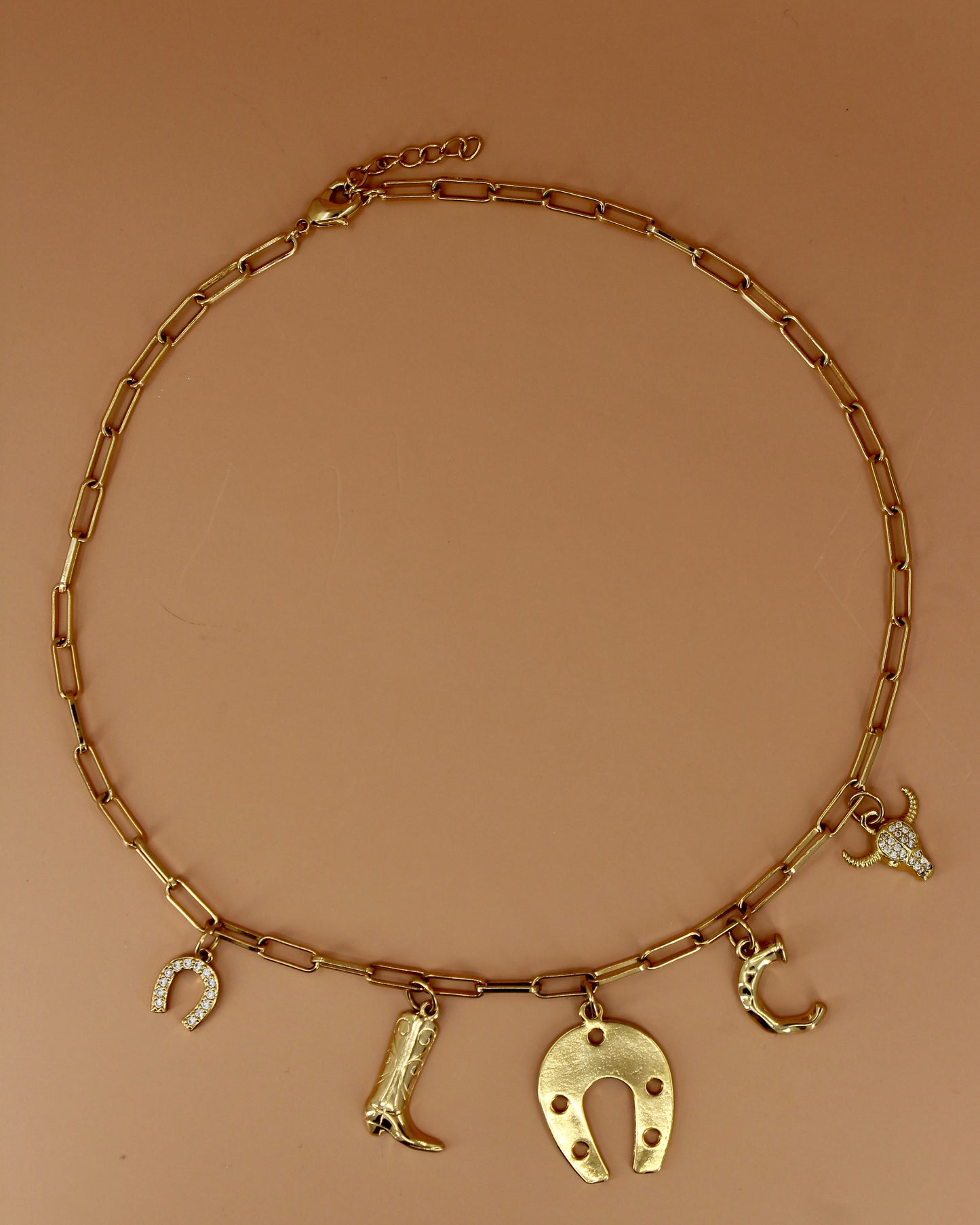 18k gold plated Western charm necklace with customizable initial, horseshoe, cowboy boot, bull skull, and paperclip chain, bold cowgirl jewelry by Cuya.