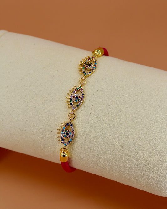 Adjustable cord bracelet with three gold and enamel evil eye charms, handmade coastal jewelry by Cuya, available in multiple colors.