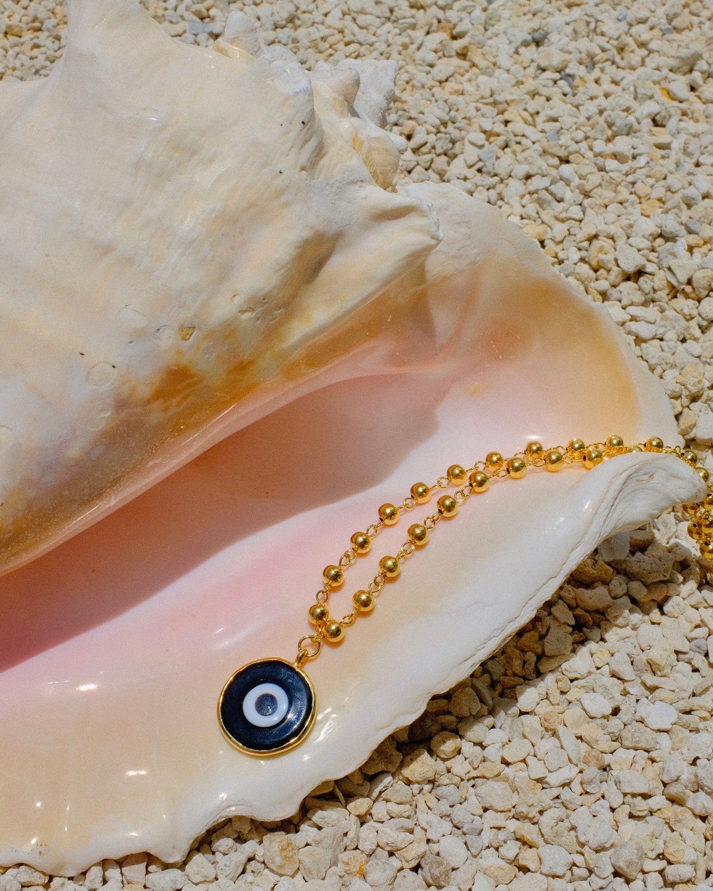Gold beaded necklace with a black eye pendant inside a shell gold plated