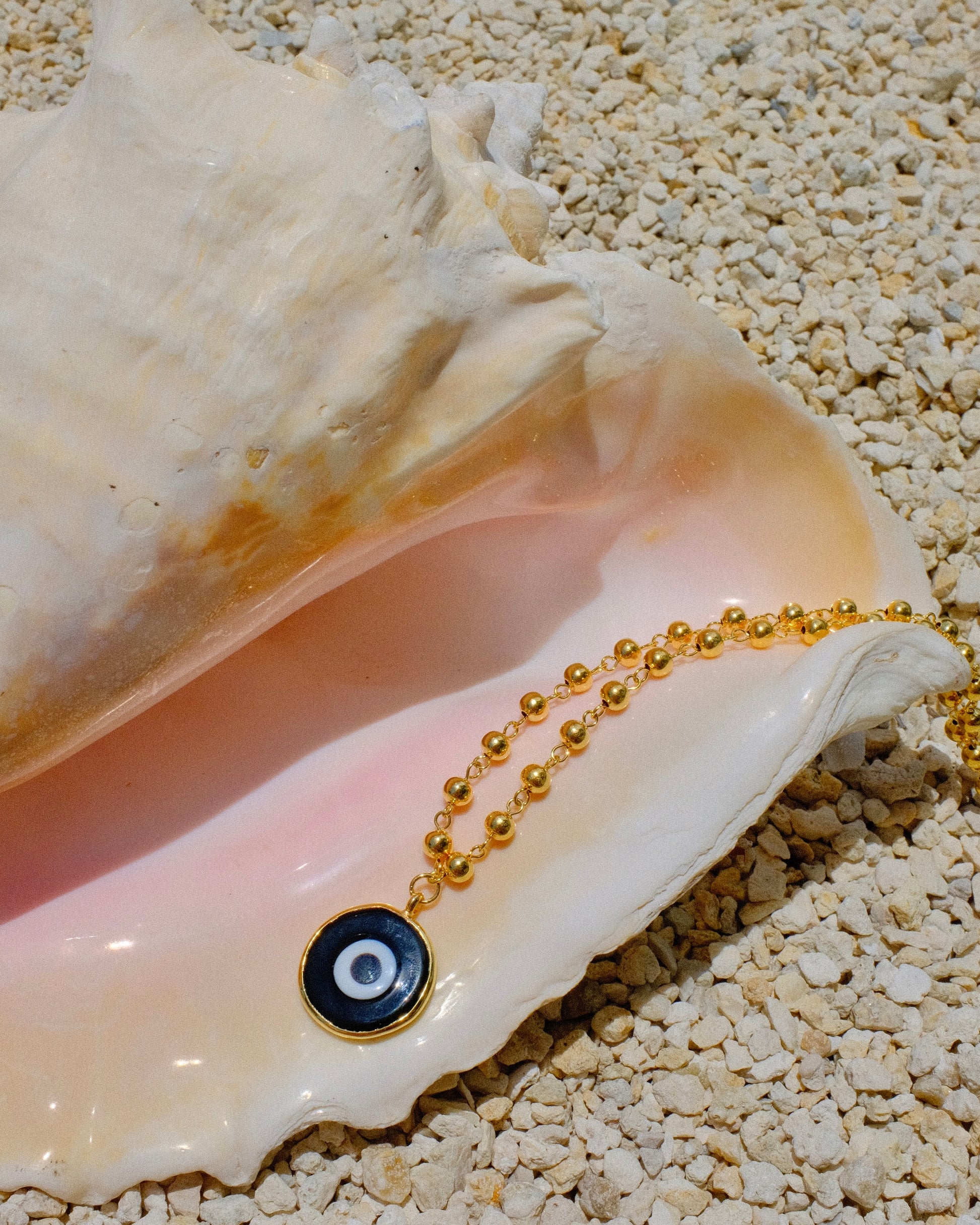 Gold beaded necklace with a black eye pendant inside a shell gold plated