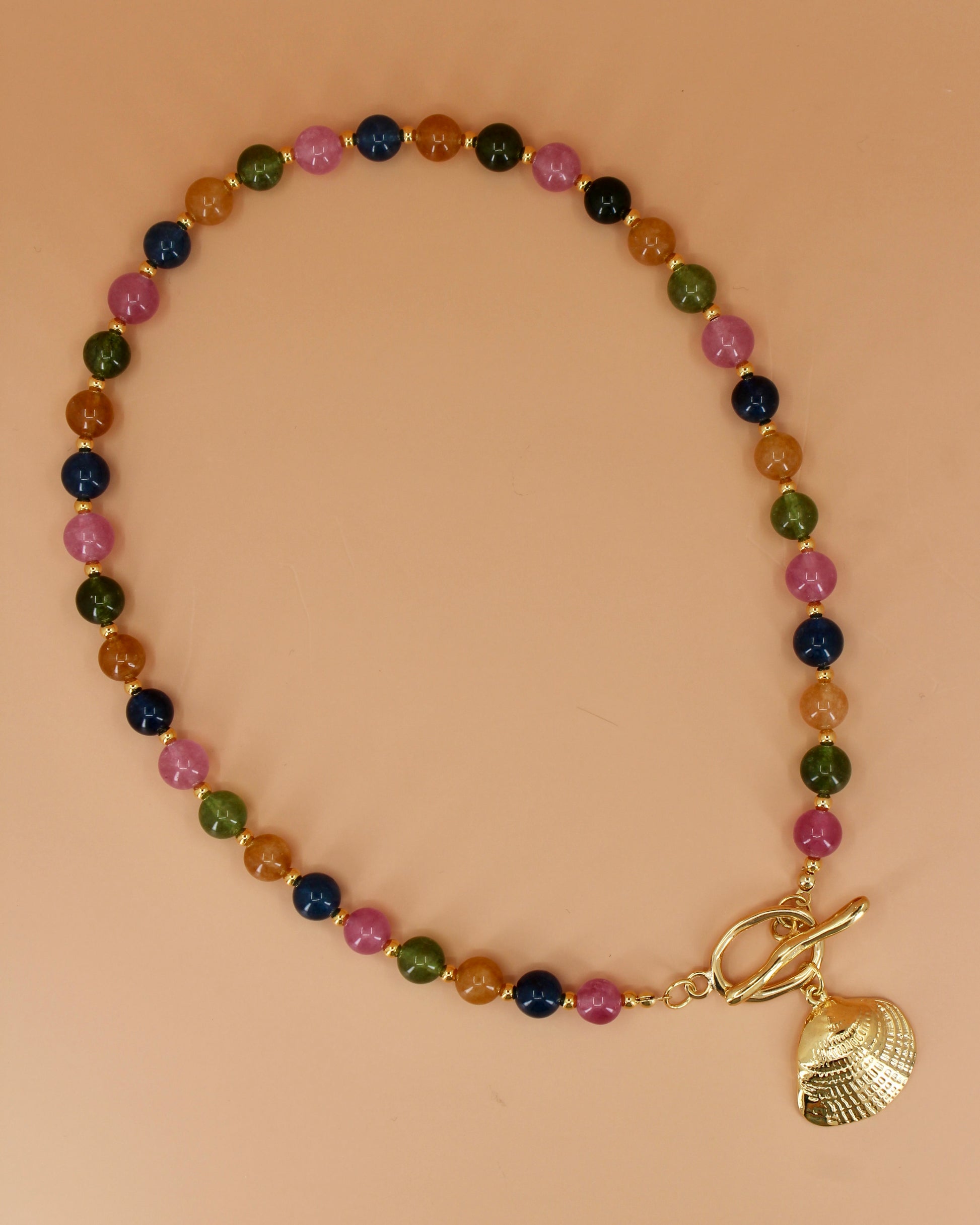 Multicolored beaded bracelet with a gold shell charm on a beige background