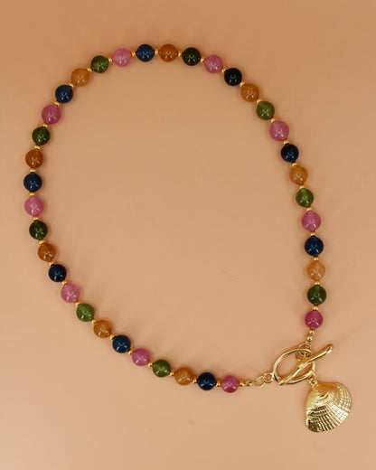 Multicolored beaded bracelet with a gold shell charm on a beige background