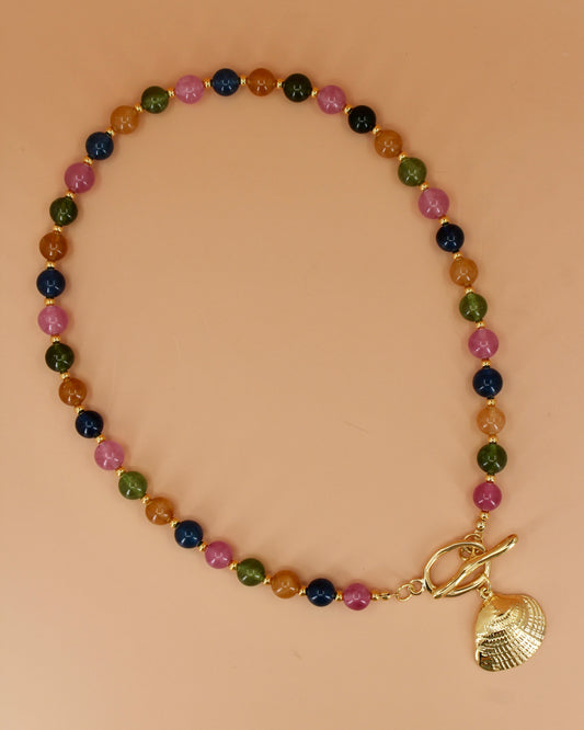 Multicolored beaded bracelet with a gold shell charm on a beige background