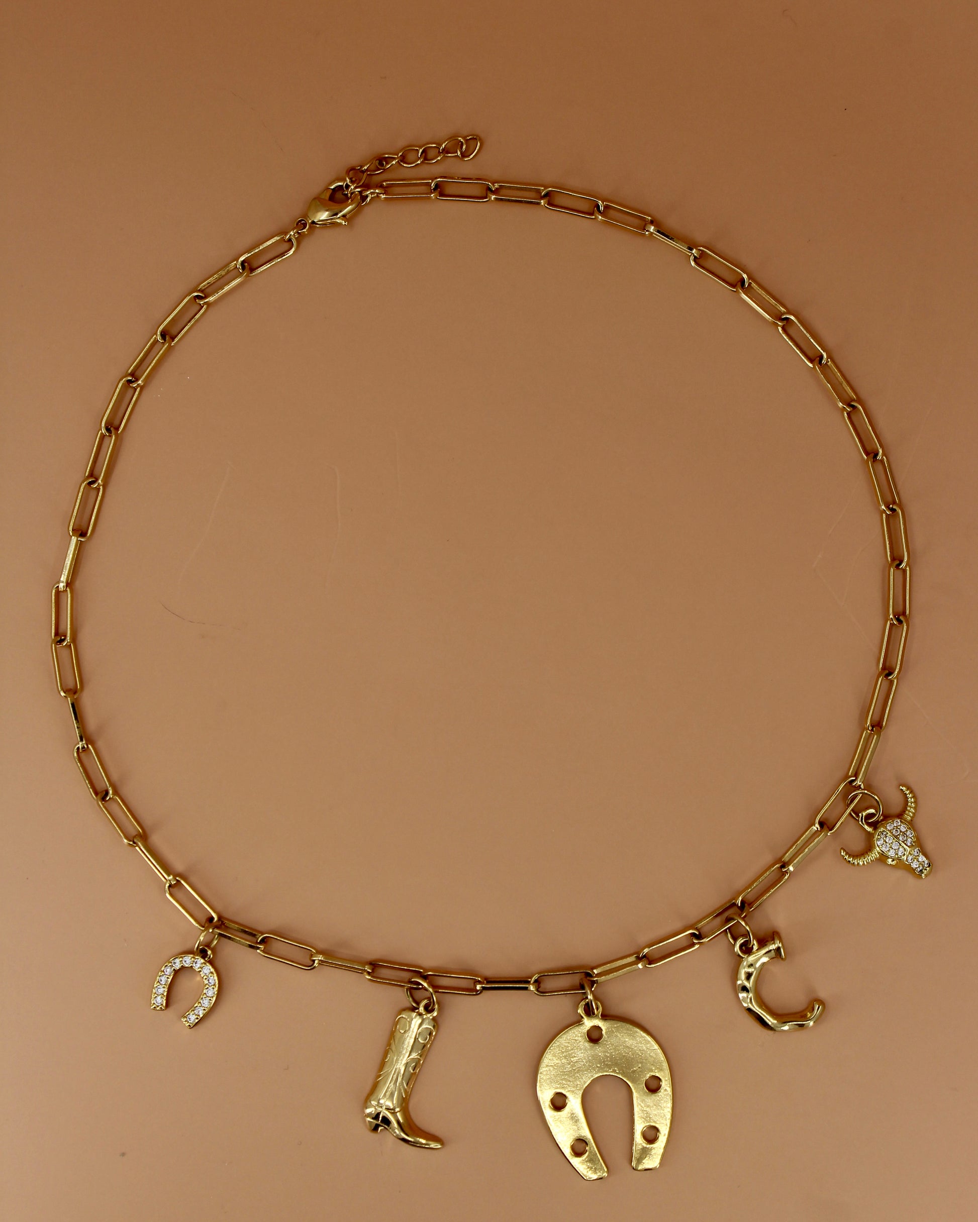 18k gold plated Western charm necklace with customizable initial, horseshoe, cowboy boot, bull skull, and paperclip chain, bold cowgirl jewelry by Cuya.
