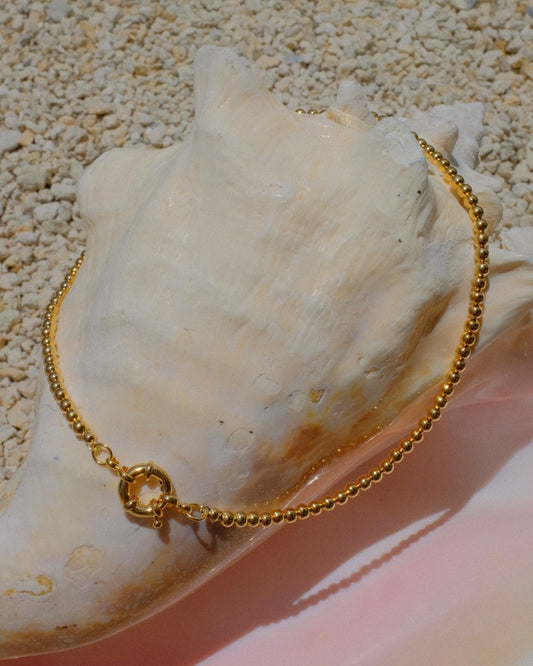 Elegant in its simplicity, the Cove Necklace features a seamless strand of polished gold&nbsp; beads, secured with a timeless circular sailor clasp. Understated yet radiant, it’s the kind of essential that elevates every outfit — from casual daywear to evening chic. Let your style shine with this piece — timeless, refined, and effortlessly graceful.