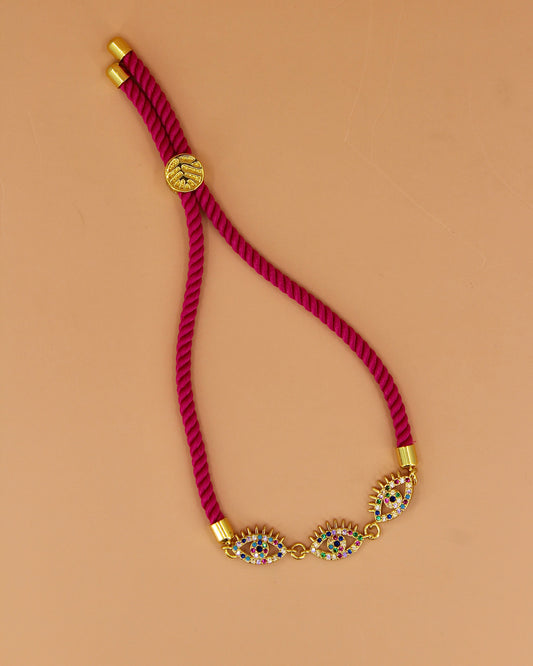 Adjustable cord bracelet with three gold and enamel evil eye charms, handmade coastal jewelry by Cuya, available in multiple colors.