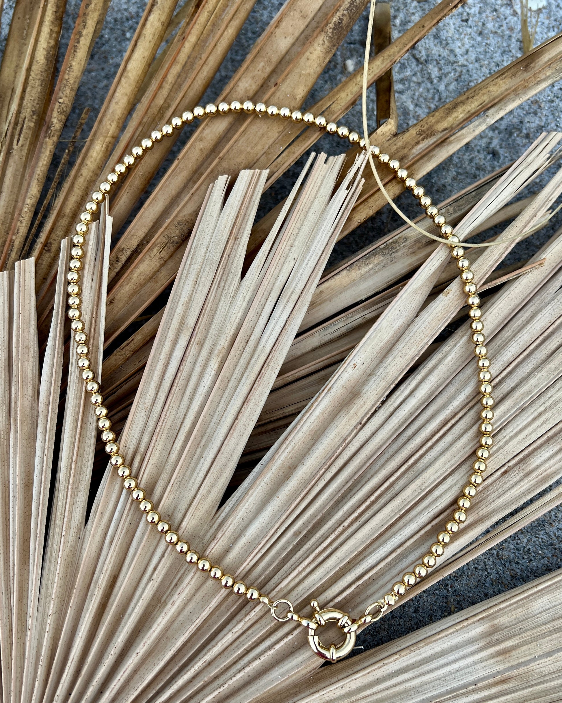 Elegant in its simplicity, the Cove Necklace features a seamless strand of polished gold&nbsp; beads, secured with a timeless circular sailor clasp. Understated yet radiant, it’s the kind of essential that elevates every outfit — from casual daywear to evening chic. Let your style shine with this piece — timeless, refined, and effortlessly graceful.