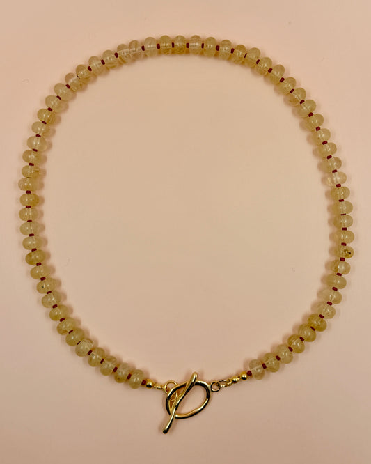 Handcrafted clear gemstone necklace with red accent beads and a gold plated toggle clasp. The IO Necklace is available in 17 inches.