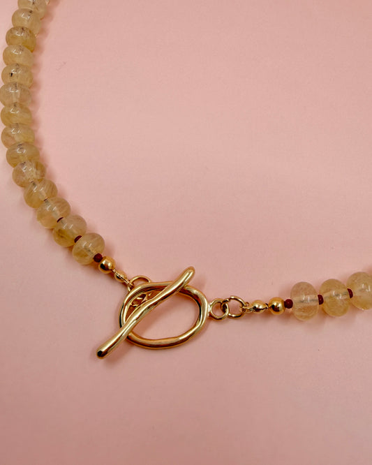 Handcrafted clear gemstone necklace with red accent beads and a gold plated toggle clasp. The IO Necklace is available in 17 inches.