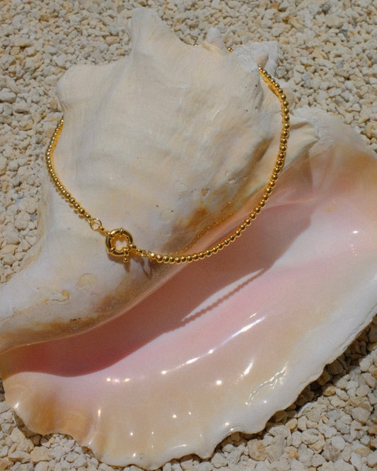 Elegant in its simplicity, the Cove Necklace features a seamless strand of polished gold&nbsp; beads, secured with a timeless circular sailor clasp. Understated yet radiant, it’s the kind of essential that elevates every outfit — from casual daywear to evening chic. Let your style shine with this piece — timeless, refined, and effortlessly graceful.
