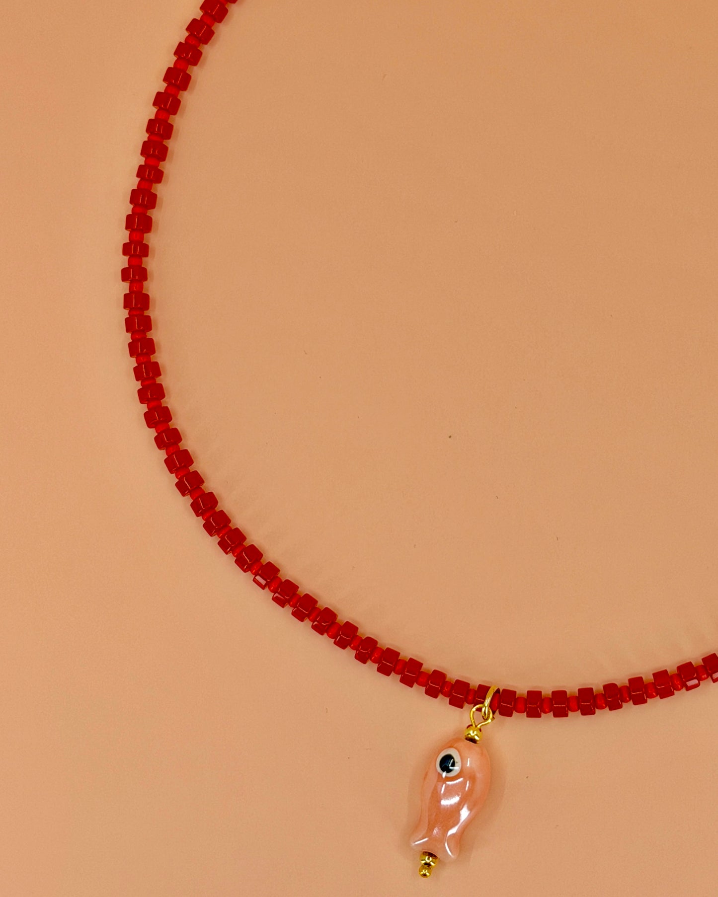 Handcrafted red gemstone necklace with a pink ceramic fish pendant. The Riva Necklace is available in 16”, 18”, and 20” lengths.