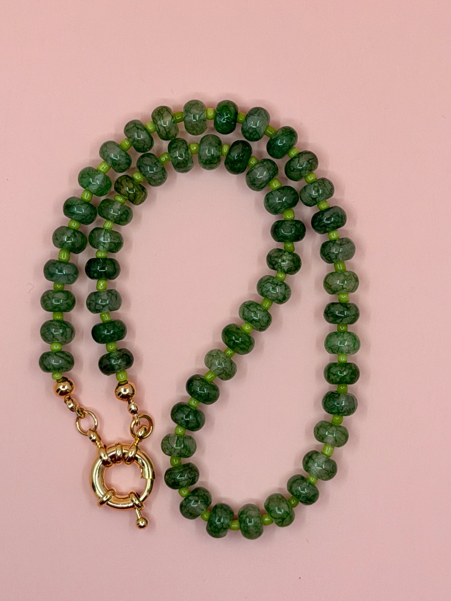 Green beaded necklace with a gold clasp on a pink background