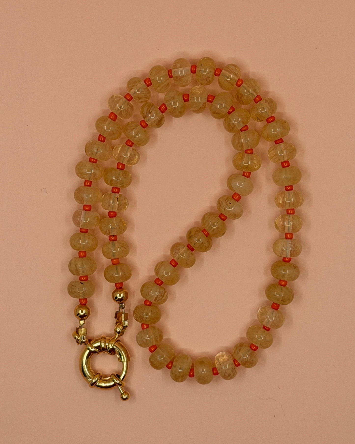Beaded necklace with a gold clasp on a pink background