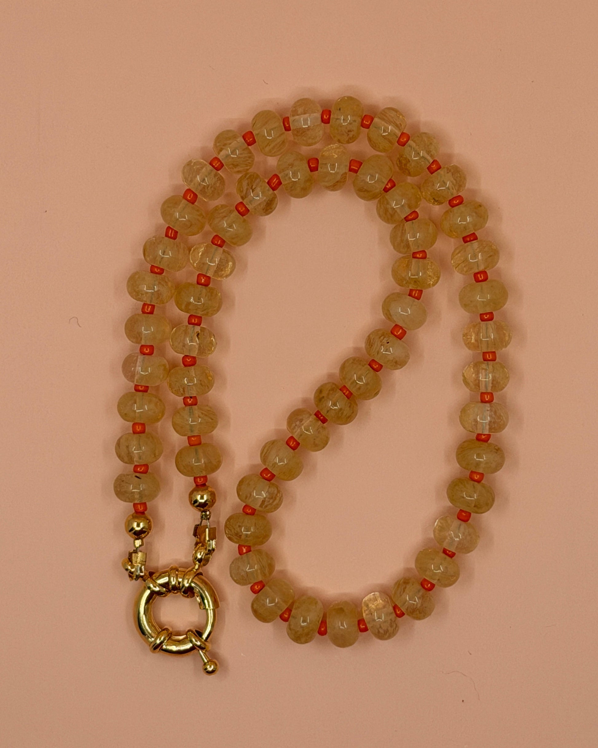 Beaded necklace with a gold clasp on a pink background