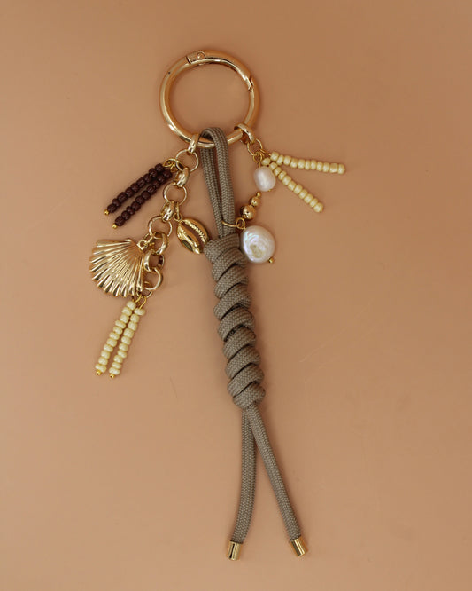 Handmade beaded keychain with gold shell, cowrie, freshwater pearl charms, and braided cord, coastal statement bag charm by Cuya.