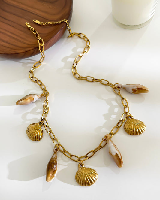 Gold chain necklace with shell pendants on a white surface